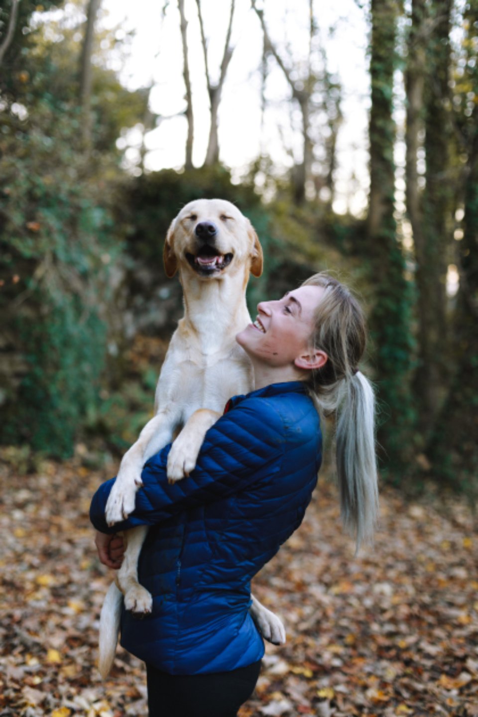 Une femme serre son chien dans ses bras, en forêt.